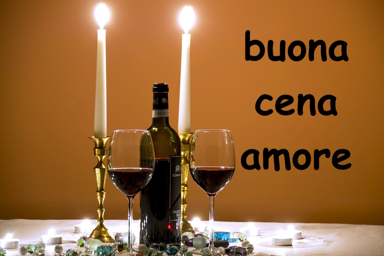  tavola romantica con due candele bianche accese e una bottiglia di vino rosso con due bicchieri 